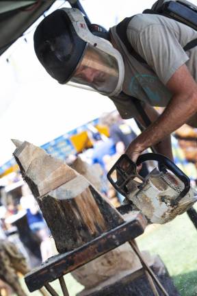 Brett McLain, owner of Freehand Custom Carvings of Fredon, uses a chainsaw to create a new sculpture in his tent. (Photo by John Hester)