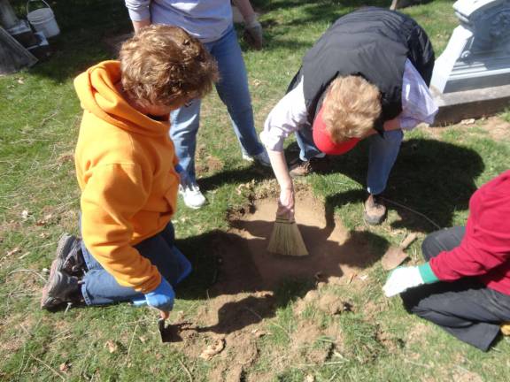 Wendy Wyman, left, and Nancy Malone brush the dirt off a freshly uncovered grave marker belonging to Garret Van Blarcum. PhotoS by Scott Baker