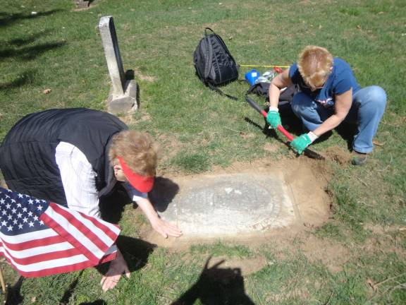 Nancy Malone, left, and Lisa Permunian work to uncover the grave marker of William Van Blarcum.