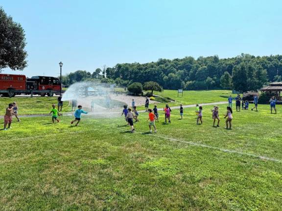 Children run through water from a fire hose after a lesson on fire safety.